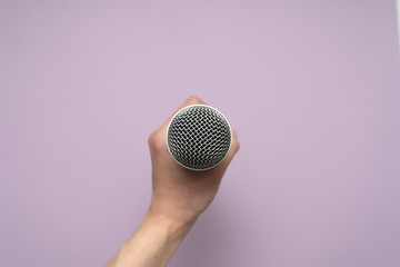 Vocal microphone in humans hand in the center of purple background. 