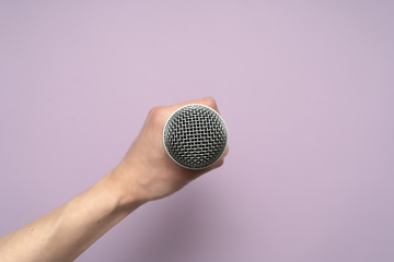 Vocal microphone in humans hand on purple background. 