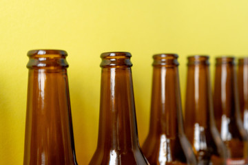 Close-up of empty beer bottles stand in a row diagonally on a yellow background.