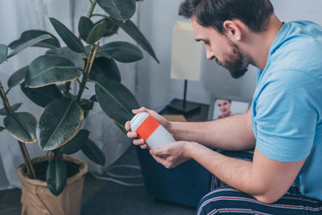 upset man sitting and looking at funeral urn at home