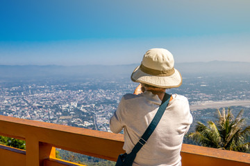 The woman is looking and taking photo to the city and mountain view from the balcony in Chiang Mai province , Thailand. 