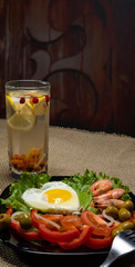 A glass with berry juice, a plate with scrambled eggs, shrimps and vegetable salad on a table against a dark background. Place for inscription.