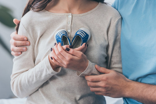 Partial View Of Parents Holding Baby Shoes At Home