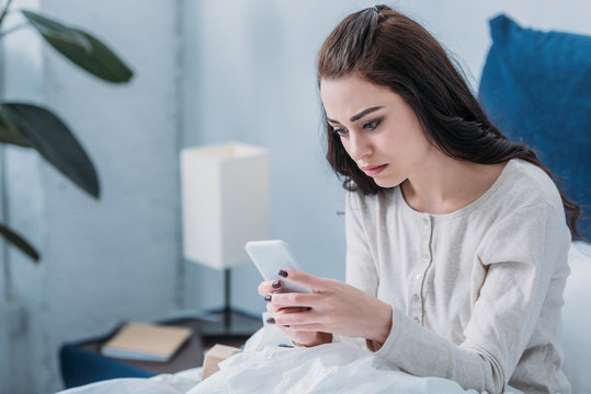selective focus of depressed woman lying in bed and using smartphone