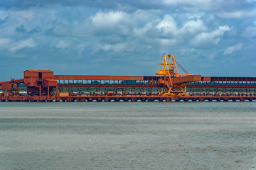 Fototapeta na wymiar Outdoor industrial jetty at sea bank with incline large conveyor for transportation bauxite ore from mining shuttle trains to feeder ships. Guinea, West Africa.