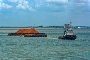 Tug boat with a large cargo barge transporting bauxite ore in Kamsar, Guinea.
