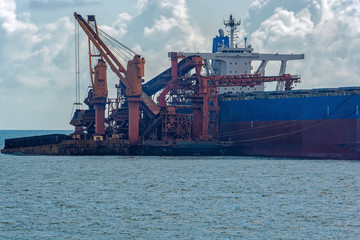 Loading ocean-going bulk carrier ship with Bauxite aluminum ore from the mini bulk carrier (feeder) vessel at offshore Kamsar port, Guinea, West Africa.