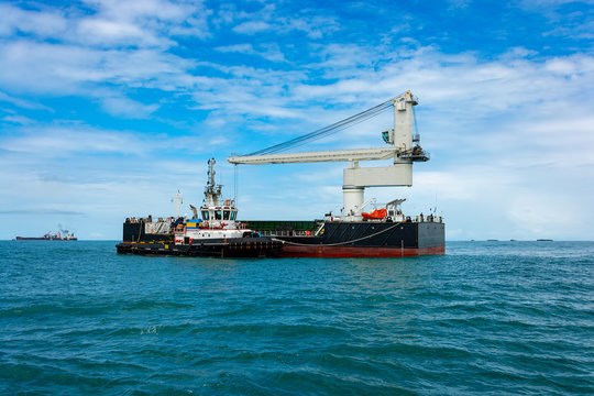 Tugboat assists Floating Crane Transhipper in bauxite transshipment operations at anchorage off Port Kamsar, Guinea.