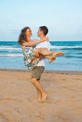 Very happy couple enjoy each other during sunset on the beach. Man holding woman on hands.