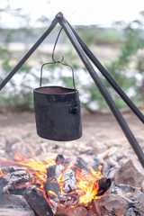 Tourist pot hanging over campfire tripod on background of river