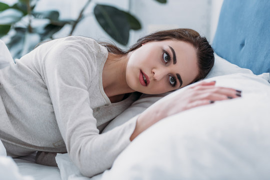 selective focus of beautiful sad woman in pajamas lying in bed at home