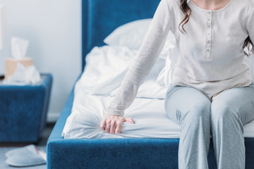 cropped view of woman in pajamas sitting on bed with copy space