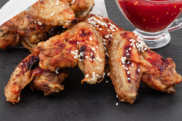 Baked chicken wings with sesame seeds and sweet chili sauce on dark background