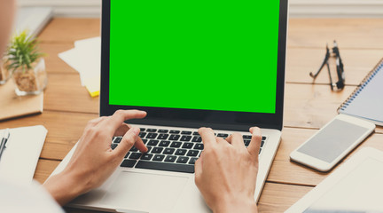 Millennial man working on laptop with blank green screen