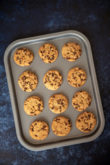Vertical image of chocolate chip cookies on a baking tray, taken on a dark blue background