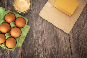 Cake ingredients, eggs, flour and butter on a wooden table with copy space