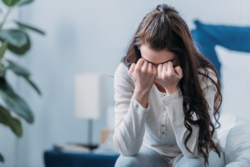 selective focus of grieving woman covering face with hands and crying at home