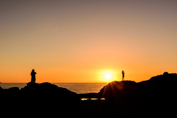 Fototapeta premium Silhouette People Standing On Rock By Sea Against Clear Sky During Sunset