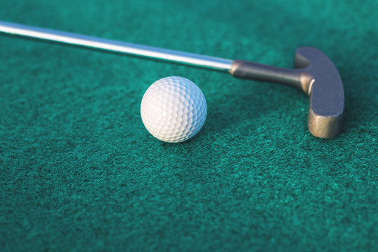 Mini golf two-way putter club and a ball on green surface close up with copy space