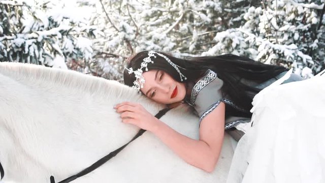 dark-haired girl gently and tenderly falls on a white horse, softly strokes animal hair and smiles mysteriously, a fallen angel in love takes the bright side, a lady with black hair and a gray cloak