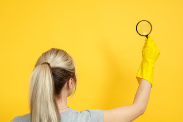 Housekeeping. Cleaning services. Woman with magnifier. Hand in rubber glove. Copy space on yellow background.