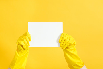 Home cleaning to do list. Hands in rubber gloves holding blank paper mockup. Copy space on yellow background.