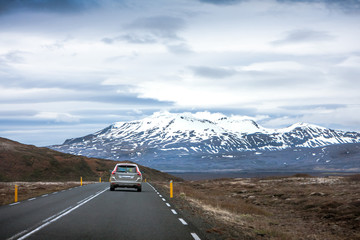 The car rides on the highway with a beautiful view of the sky and snow-covered mountain, Iceland