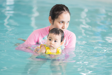 Fototapeta na wymiar Mother and asian baby girl swimming in a pool, early development class for infants swimming. Baby swimming concept.