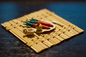 Plasticine crafts on a bamboo mat. Carrots, apple with a worm, a plate, circling and a spoon.