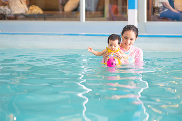 Asian baby girl reach for a toy in swimming pool.Baby swimming concept. Mother and baby swim in the pool.