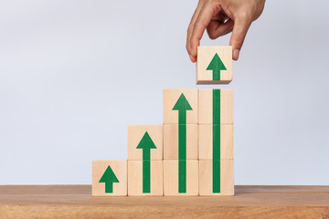 Hand arranging wooden cube stack as a graph with arrows pointing up on white background. Concept of growth and success or rising successful development and business development in the future