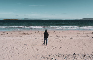 One man walking on the beach on a sunny day, showing hills and blue skies in the background. Taken on Renvyle beach along the Wild Atlantic Way in Ireland.