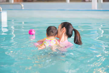 Asian baby girl reach for a toy in swimming pool.Baby swimming concept. Mother and baby swim in the pool.