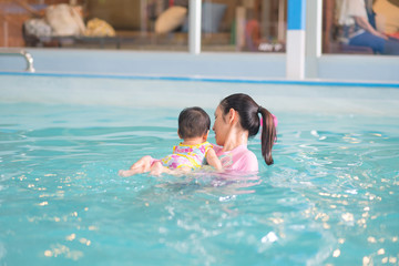 Mother and asian baby girl swimming in a pool, early development class for infants swimming. Baby swimming concept.