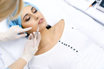 Professional cosmetologist making injection in face, lips. Young woman gets syringe with filler for face contouring or augmentation. Face aging, rejuvenation and hydration procedures