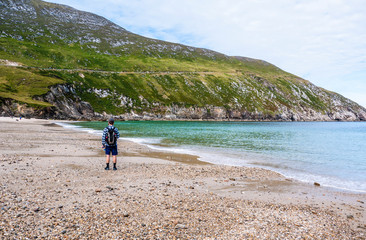 One man walking along a beautiful sandy beach surrounded by high hills on a sunny summer day. Taken in Keem Bay on Achill Island, Ireland.