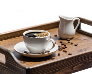 Cup of coffee with grains and milk jug on wooden tray