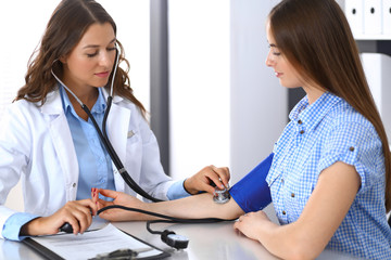 Doctor checking blood pressure of female patient while sitting at the desk in hospital office. Cardiology in medicine  and health care concept