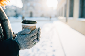 Close-up female's hands in warm gloves holding paper cup hot drink