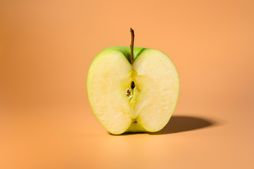 Sliced green delicious apple isolated on orange background with contrast shadows