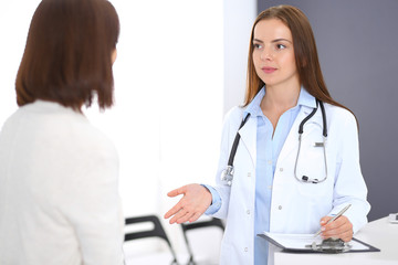 Fototapeta premium Doctor and patient discussing something while standing near reception desk in emergency hospital. Physician at work in clinic. Medicine and health care concept