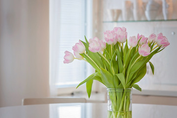 A fresh and clean home office with soft pink tulip flowers in a kitchen for Women's Day celebration. Airy Scandinavian/Nordic interior style on a media office in Finland.