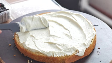 Cooking a pie stuffed with strawberries. Woman spreading a cream on the baked dough.