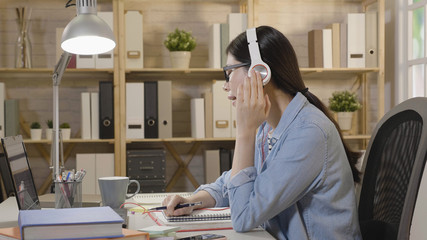 Funny happy female student sitting at desk and singing while listening to loud music through headphones connected to laptop. college girl enjoy melody of songs closing eyes relaxing while studying.