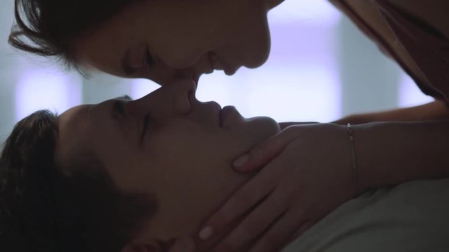 Woman face over face of her man, lying on his back. Girl rubbing noses with her boyfriend close up. Loving couple rest at home together. Leisure of young family