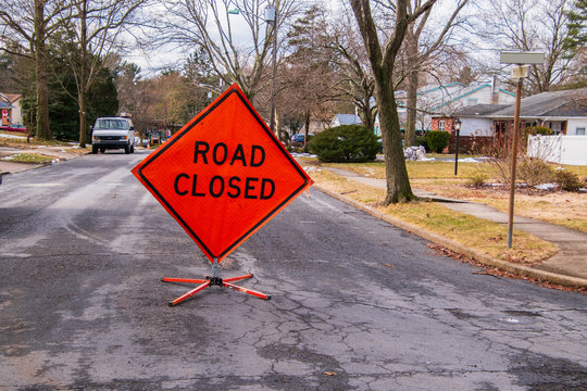 Orange diamond shaped road closure sign on road in a neighborhood near a house.