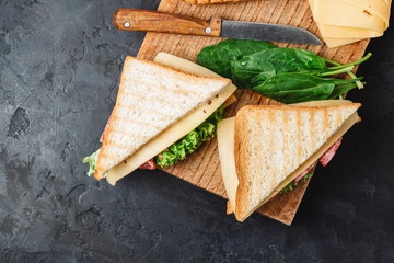 Sandwiches on a cooking board, grilled toast, salami sausage, salad lettuce and cheese on a dark background, top view