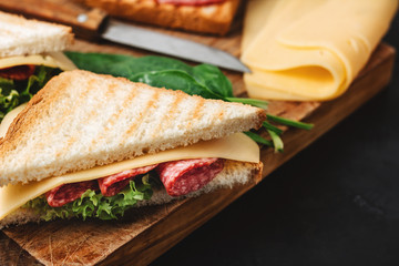 Sandwiches on a cooking board, grilled toast, salami sausage, salad lettuce and cheese on a dark background