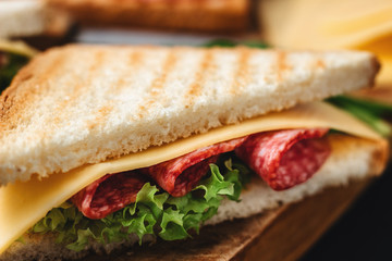 Sandwiches on a cooking board, grilled toast, salami sausage, salad lettuce and cheese close up view