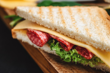 Sandwiches on a cooking board, grilled toast, salami sausage, salad lettuce and cheese close up view